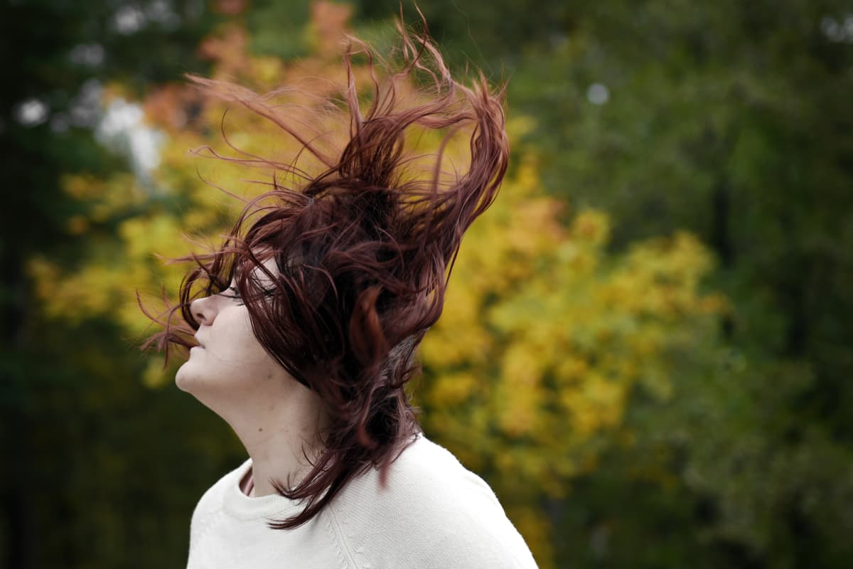 Nuori nainen seisoo hiukset hulmuten tuulessa.