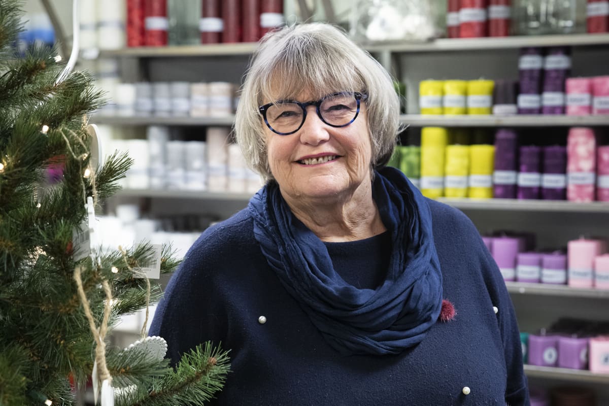 Kynttiläyrittäjä Terttu Kilpinen seisoo hymyillen myymälässään kynttilöiden ympäröimänä.