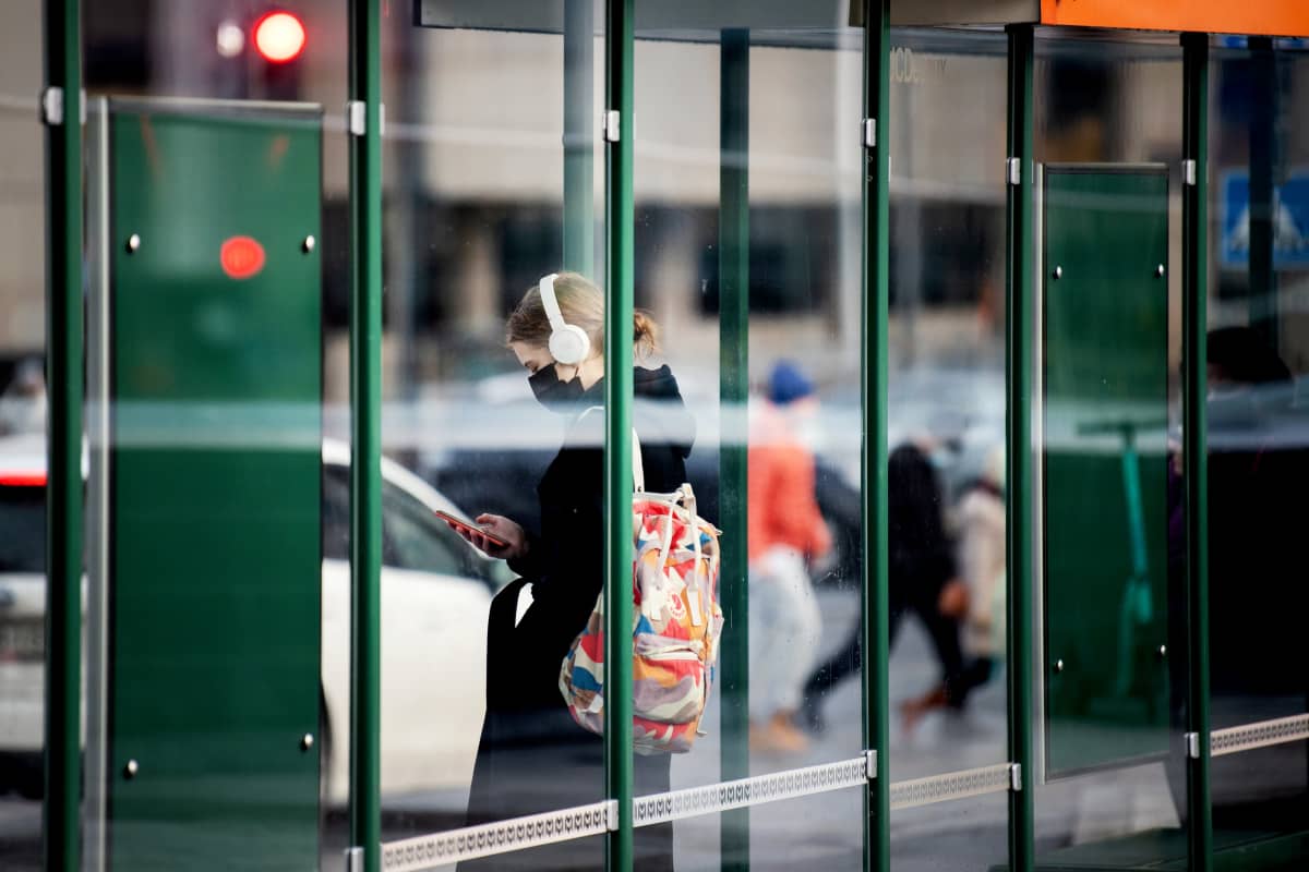 Kasvomaskia käyttävä henkilö odottaa pysäkillä raitiovaunua.