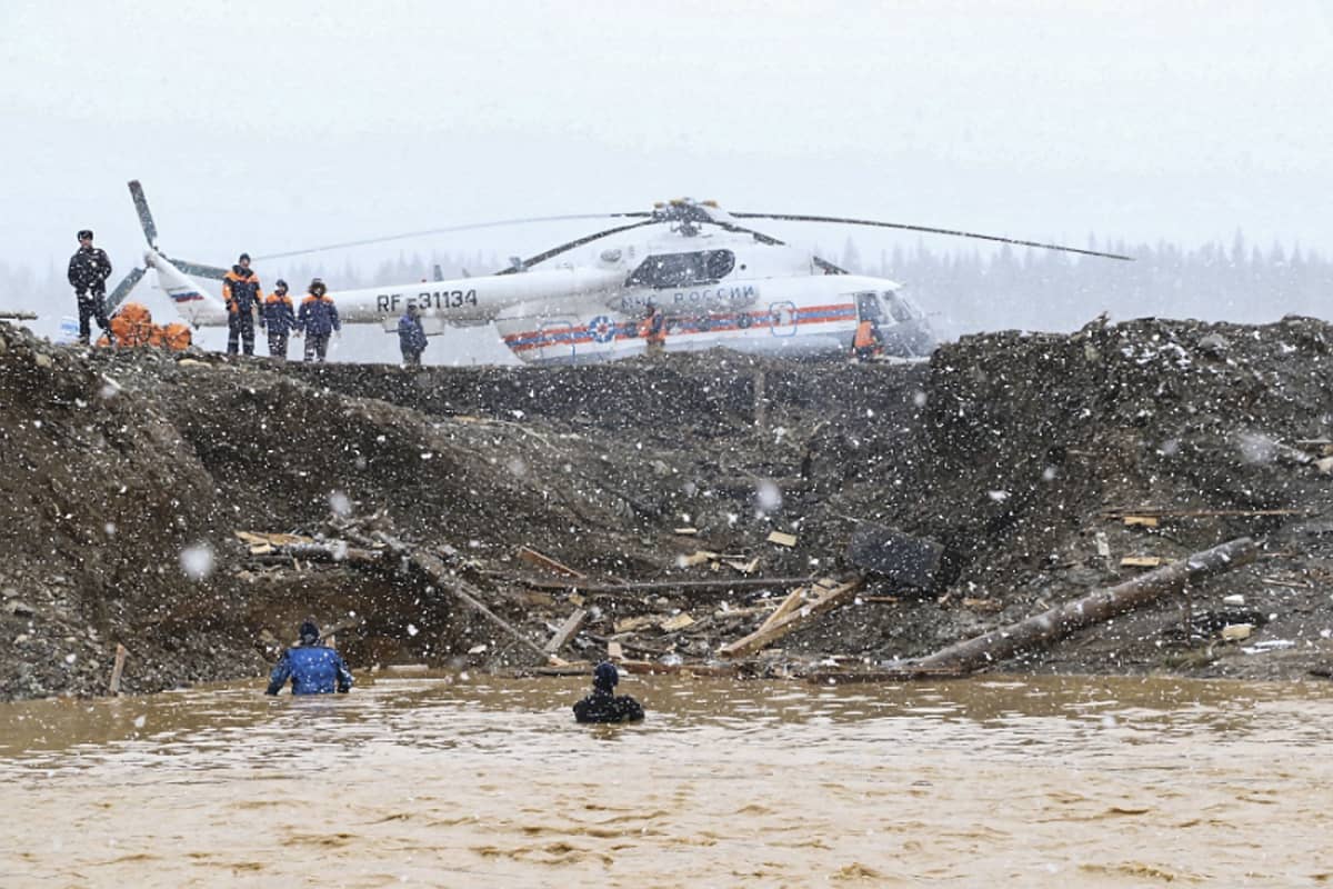 Kaksi ihmistä kahlaa syvällä vedessä. Taustalla pelastushenkilöstöä ja helikopteri.