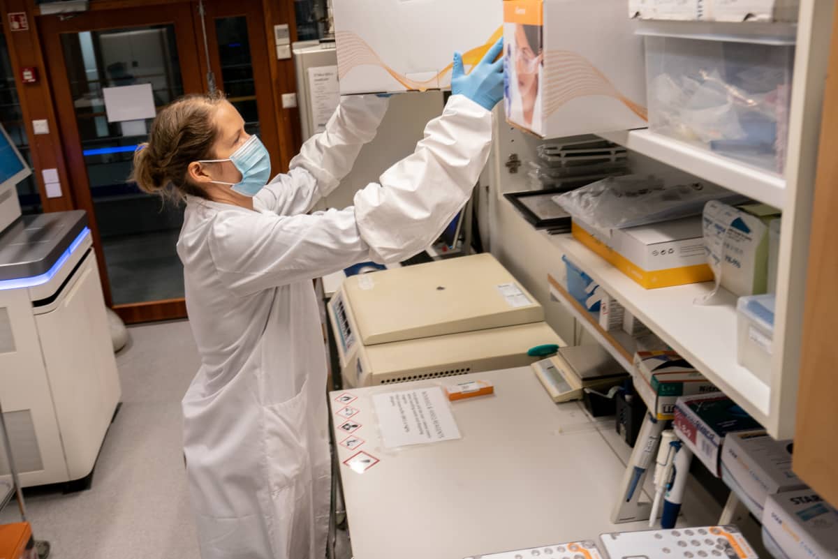 Sari Hannula ottamassa reagenssikasettilaatikkoa hyllystä FIMMin laboratoriossa.