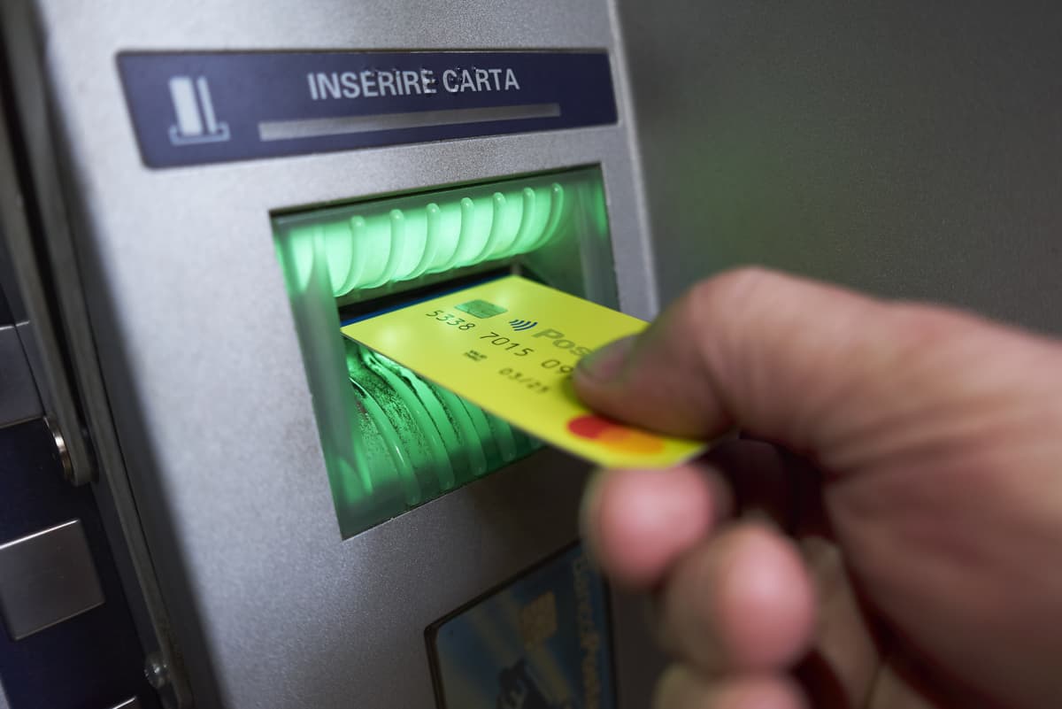 Käsi työntää keltaista muovikorttia pankkiautomaatin kortinlukijaan.