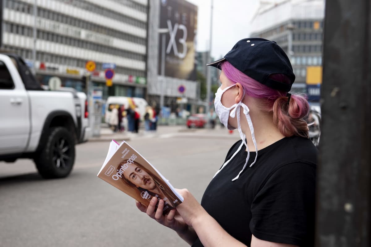 Nuori nainen lukee opinto-opasta kasvomaski naamallaan Helsingin keskustassa.