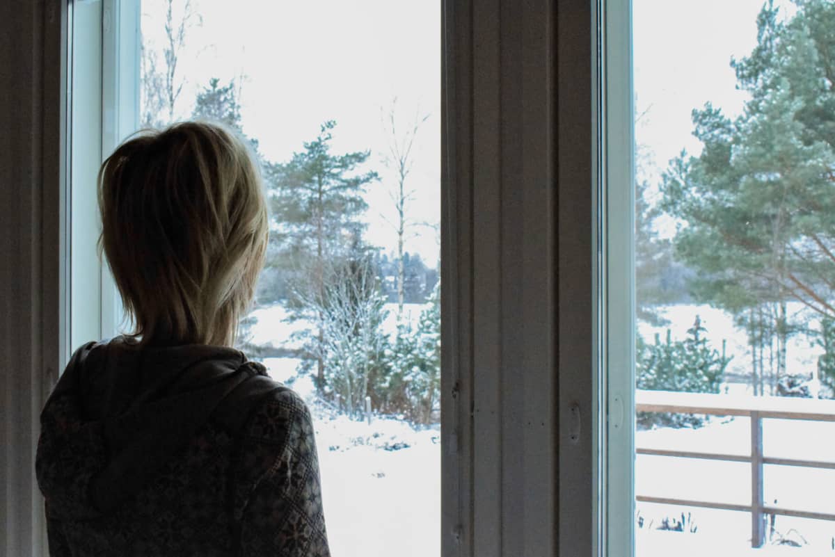 Anonyymina haastateltu henkilö katselemassa ikkunan edessä lumista talvimaisemaa. 