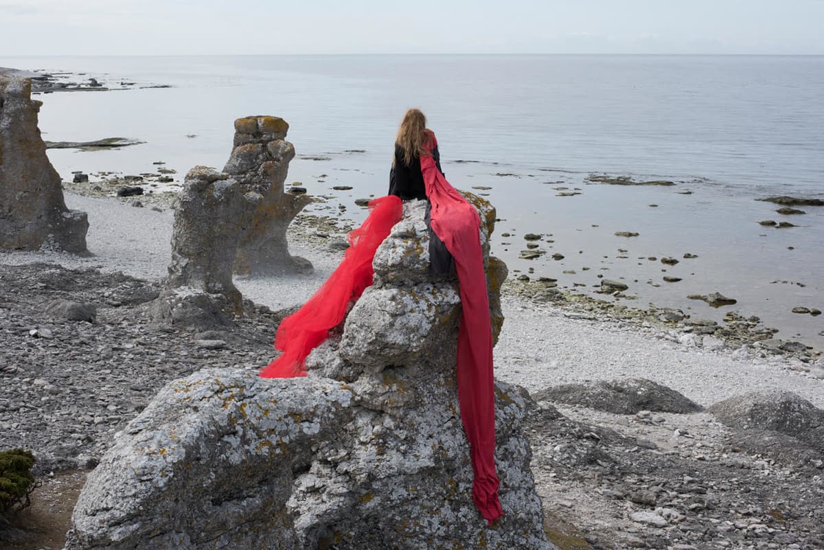 Valokuvateos, jossa nainen istuu kalliolla meren rannalla, katsellen horisonttiin.