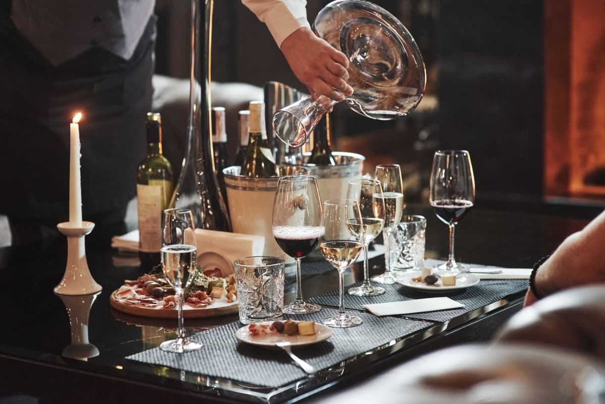 En servitör häller vin på en restaurang. På bordet står vinglas och mat.