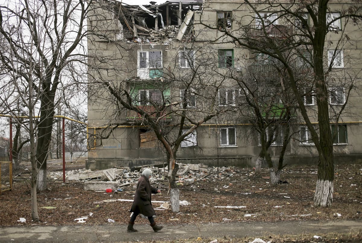 Henkilö kävelee tuhoutuneen kerrostalon ohitse.   ( A local woman walks past a damaged with shelling building in Popasne village of Luhansk area, Ukraine, 28 February 2015. Ukraine  is withdrawing heavy weapons from its front line in the east in order to test if a peace plan with separatist rebels can work, President Petro Poroshenko said 27 February 2015. The separatists say that they began the withdrawal days earlier )