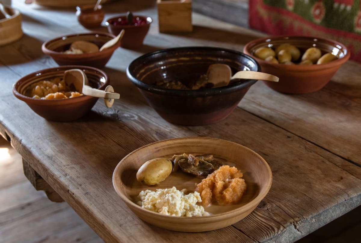 Pöydässä ruokaa, jota olisi tarjottu 1800-luvun puolivälin kievarissa; perunoita, possunpaistia, naurissosetta. 
