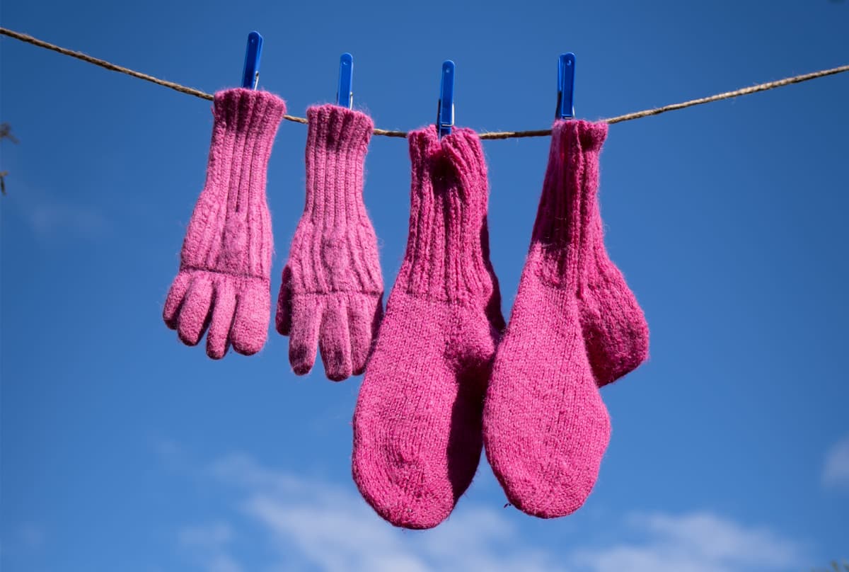 Pinkit villasormikkaat ja -sukat on ripustettu narulle kuivumaan. Takana sinistä taivasta.
