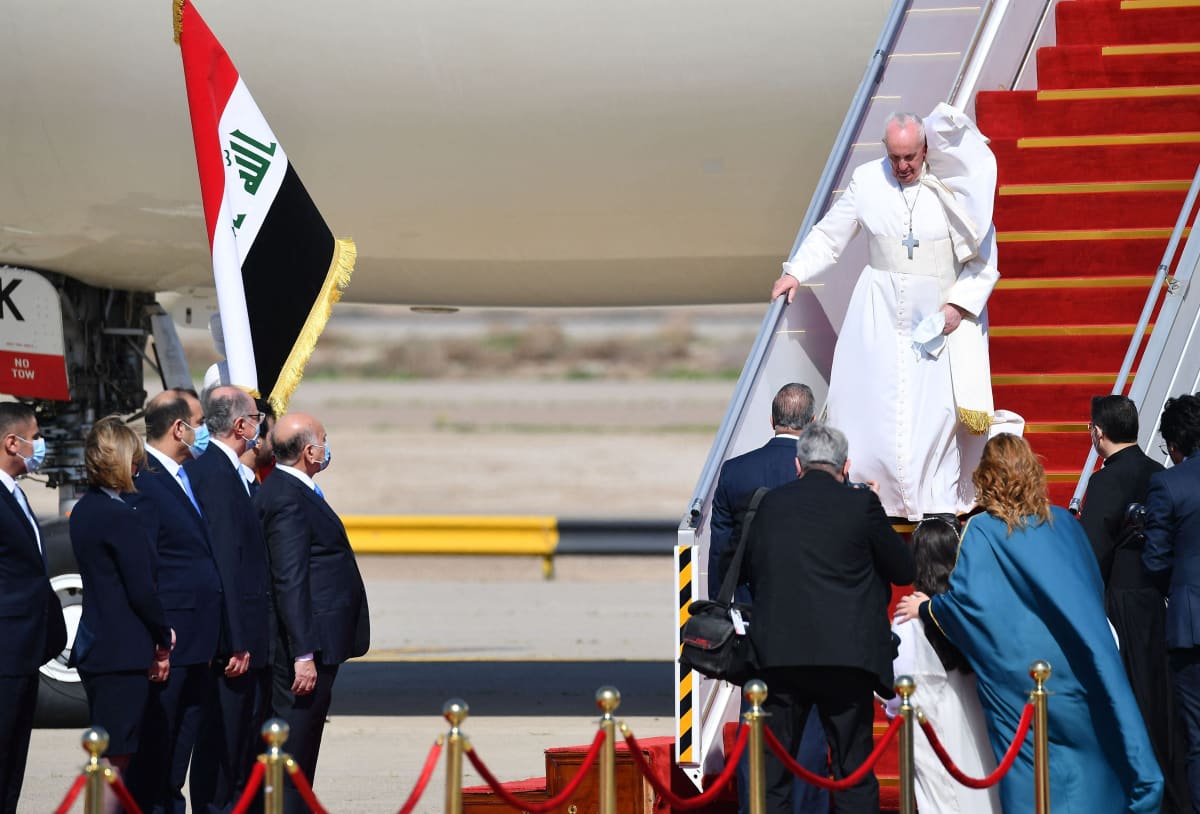 Paavi kävelee lentokoneen portaita alas, kaapu lepattaa.