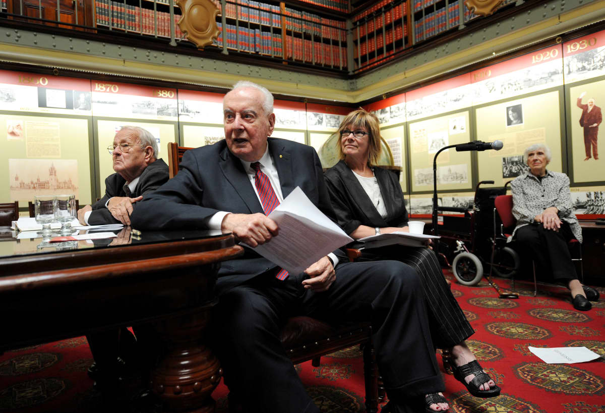 Neljä ihmistä istuu kirjastossa, etualalla papereita pitelevä Gough Whitlam