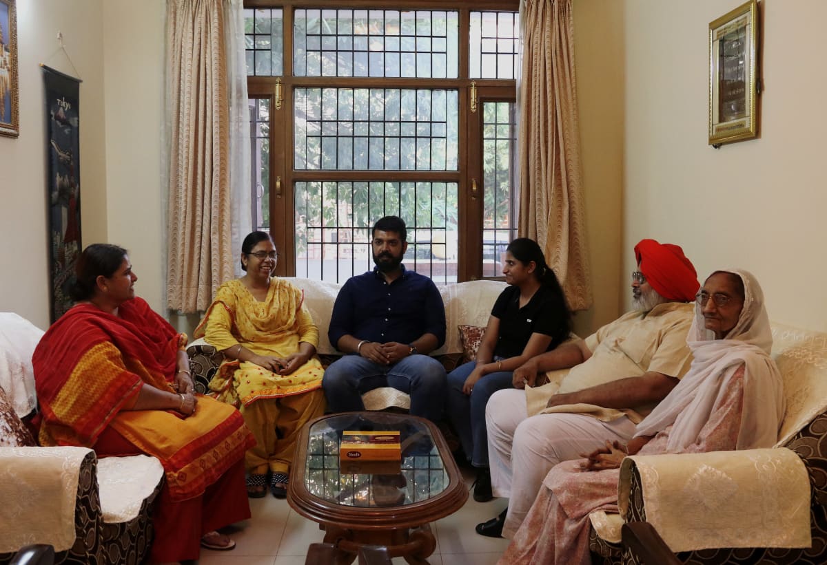 Intialainen kuusihenkinen perhe istuu sohvilla.  Kuvassa kaksi miestä ja neljä naista.  Vanhemmalla miehellä on punainen turbaani.