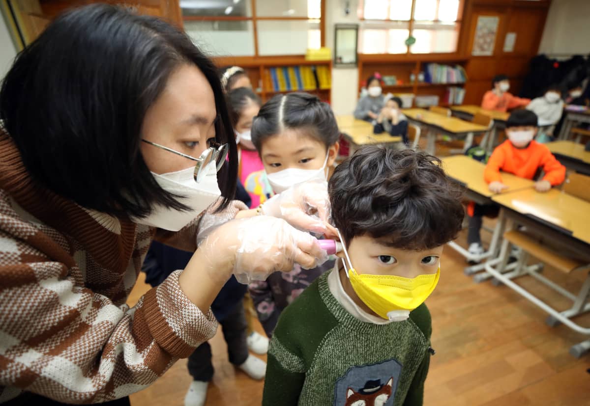 Opettaja mittaa hengityssuojaimeen pukeutuneelta oppilaalta kuumeen Soulissa Etelä-Koreassa 30. tammikuuta 2020.