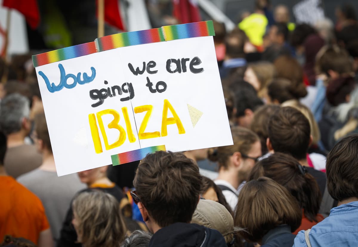 Ihmiset osoittivat mieltään. Yhden protestoijan kyltissä lukee 'Wow we are going to Ibiza'.