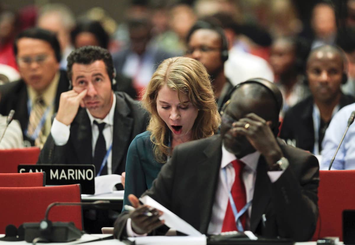 Maailman maiden edustajat istuvat ilmastokokouksessa. Yksi edustajista haukottelee.