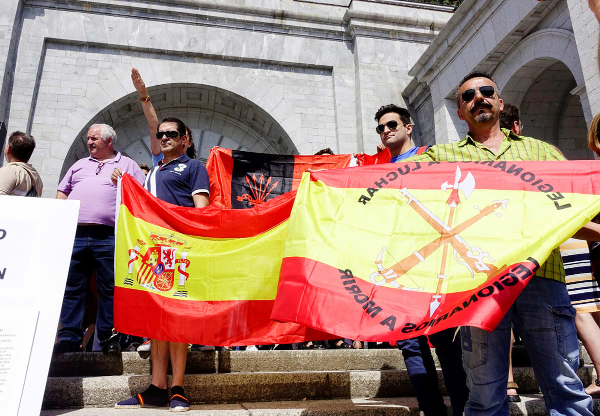 Miehiä iskulauseiden ja Espanjan lipun kanssa, taustalla henkilö tekee fasistitervehdystä.