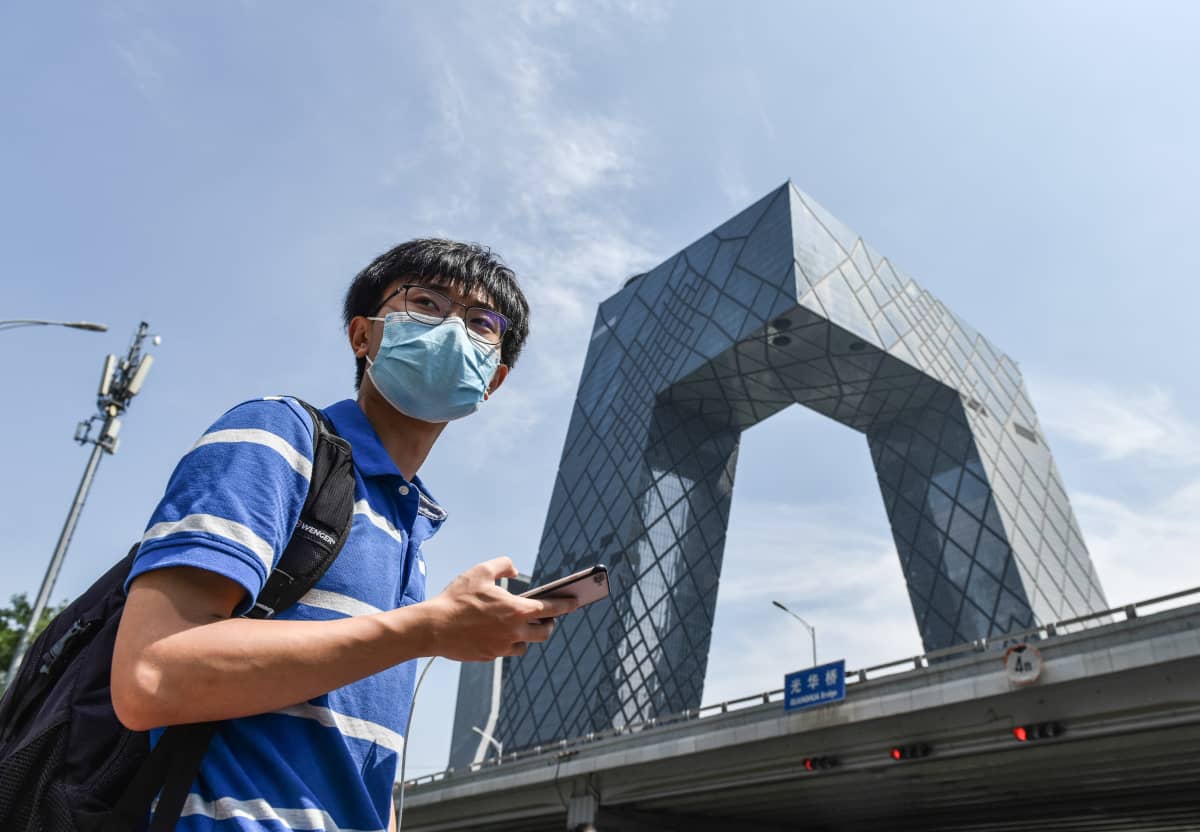 Nuori mies kännykkä kädessä. Taustalla näkyy Kiinan valtion tv:n CCTV:n rakennus.
