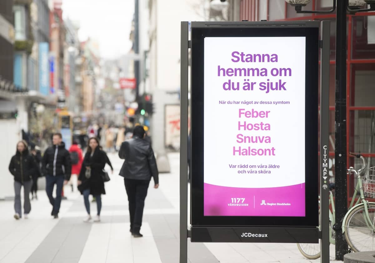 Mainostaulu Drottninggatanin kävelykadulla, taustalla ihmisiä.