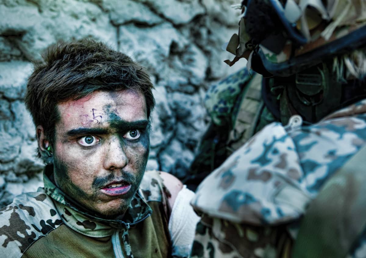 Hieman kauhistuneen näköinen sotilas katsoo silmä suurina hänellä on naamioväriä tai likaa kasvoissaan. 