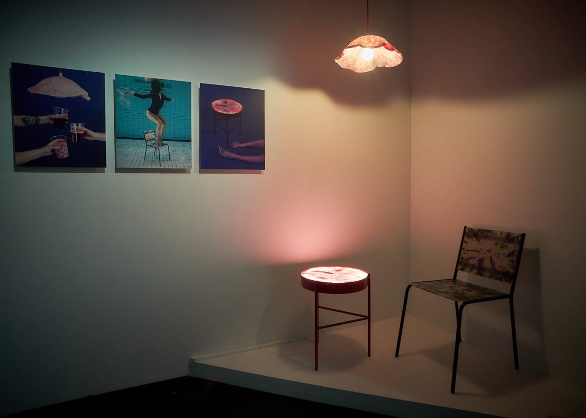Valokuvia seinällä, valaisin, pöytä ja tuoli
