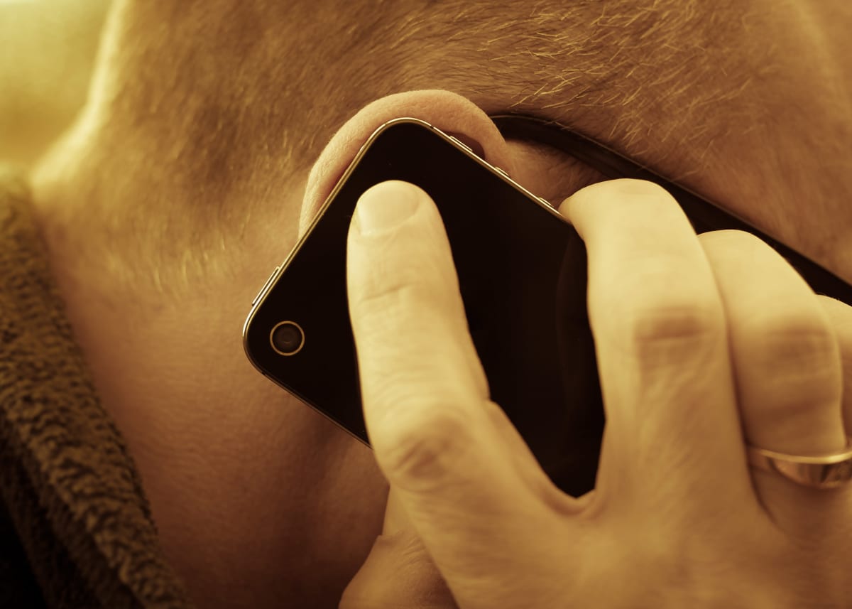 En närbild på en man som talar i en mobiltelefon. Mobilen och mannens hand täcker hans öra. 