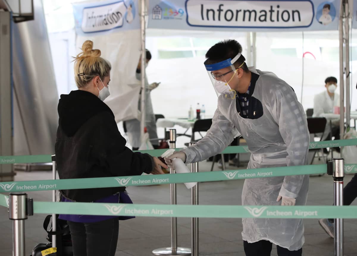 Suojavarusteisiin pukeutunut virkailija ottaa koronavirustestin eurooppalaislta matkailijalta lentokentällä Etelä-Koreassa.