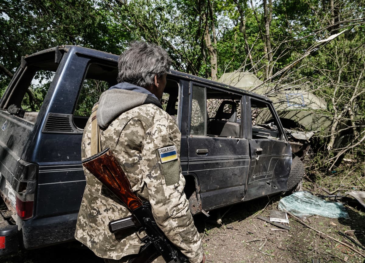 Ukrainalainen sotilas tuhoutuneen auton edessä.