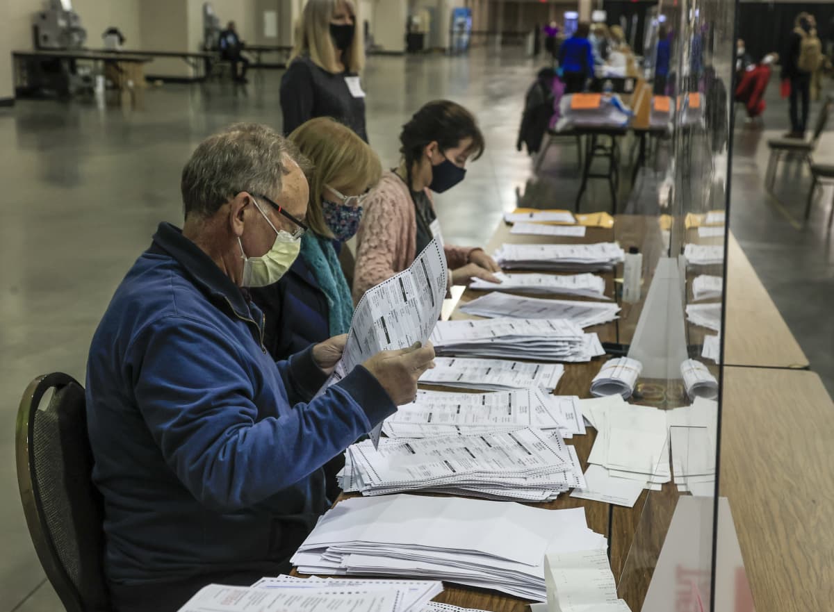 Kolme ääntelaskijaa kasvomaskeissa käsittelee vaalilippuja Wisconsinissa. 