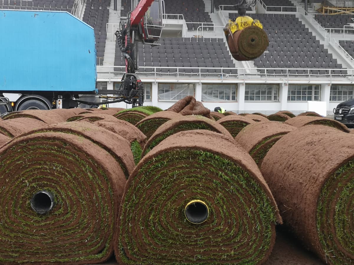 Olympiastadionille asennetaan siirtonurmea. Kuvassa isoja nurmirullia lastataan kuorma-auton lavalta stadionin kentälle.