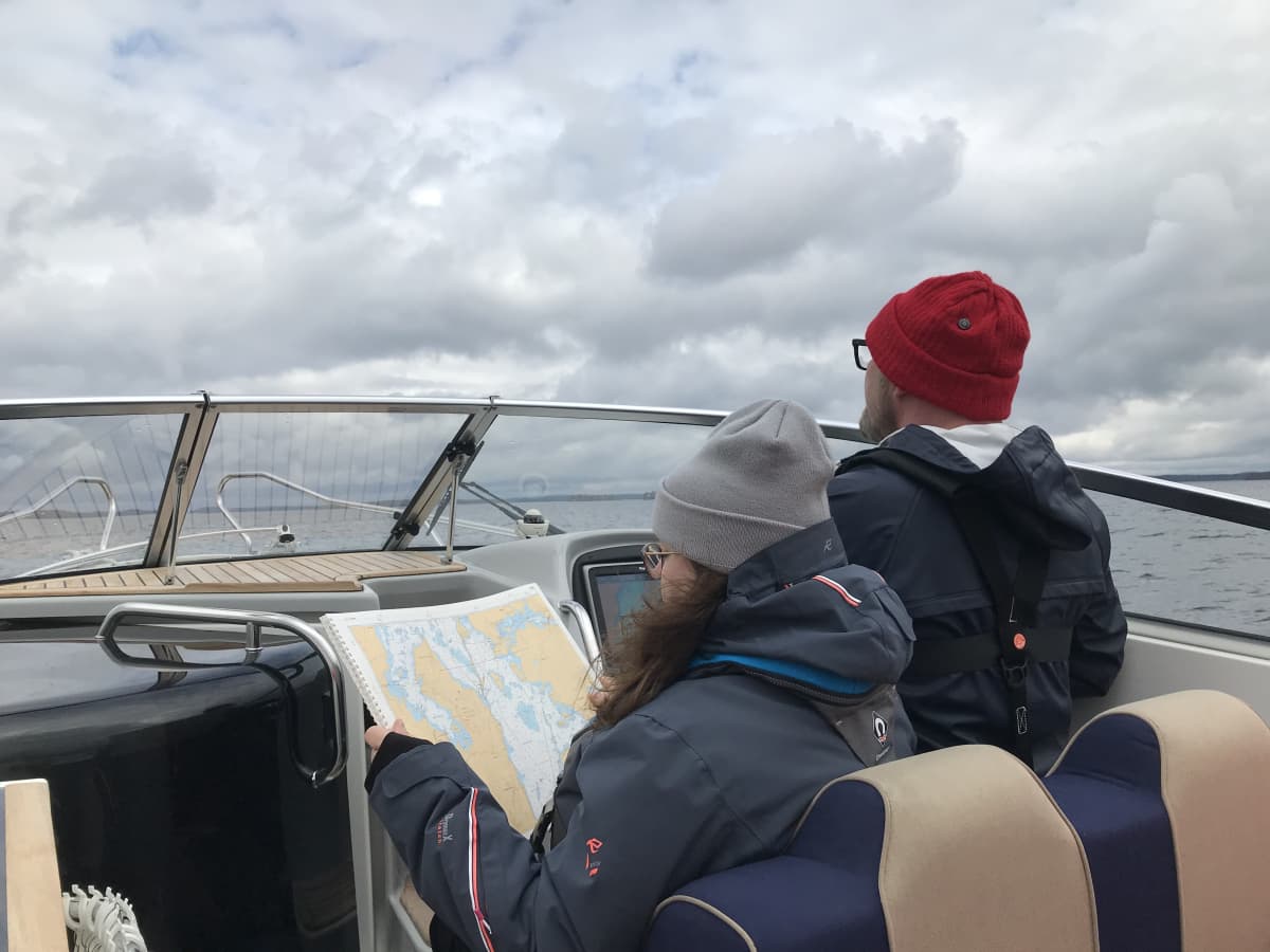 Nainen lukee karttaa veneessä, jota mies ohjaa Vesijärvellä.