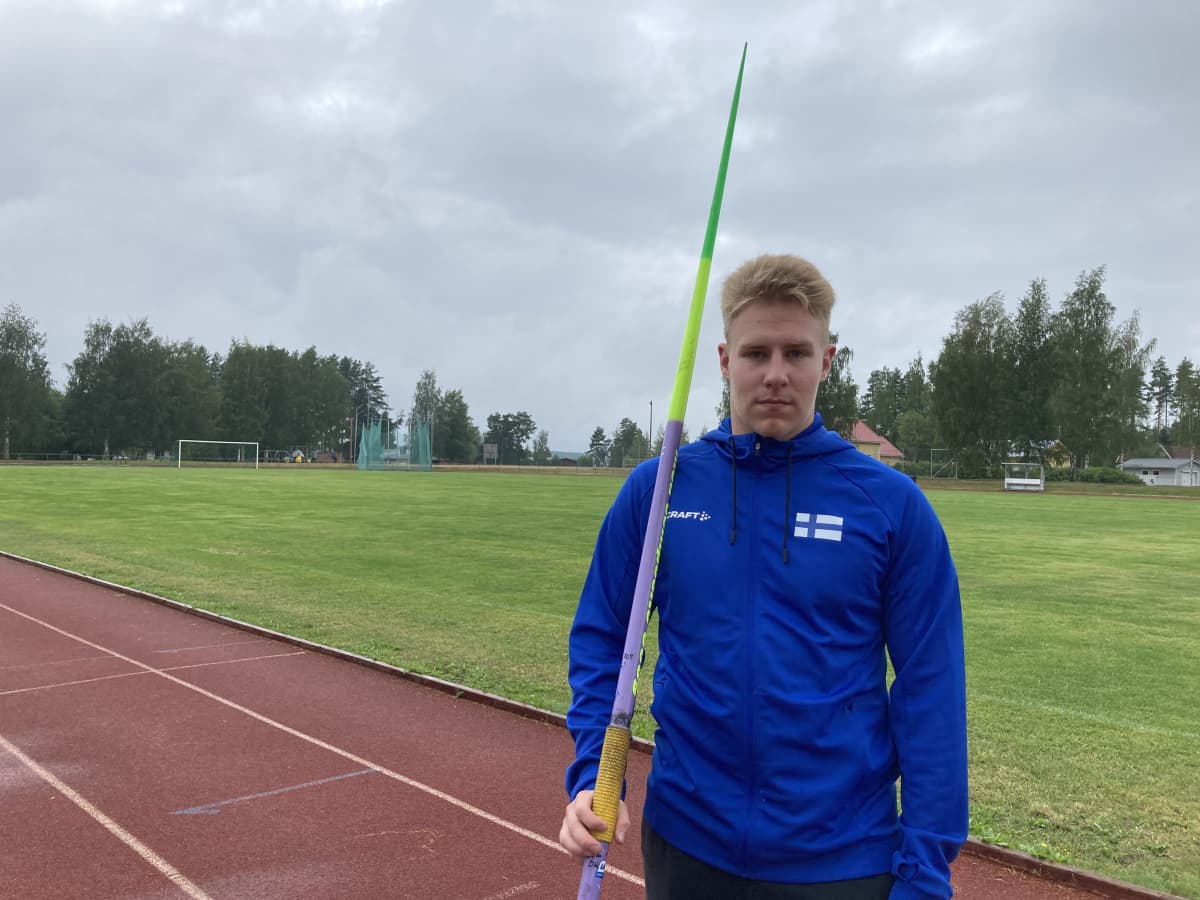 Veteliläinen keihäänheittäjä Janne Läspä seisoo urheilukentän laidalla keihäs kainalossa. 