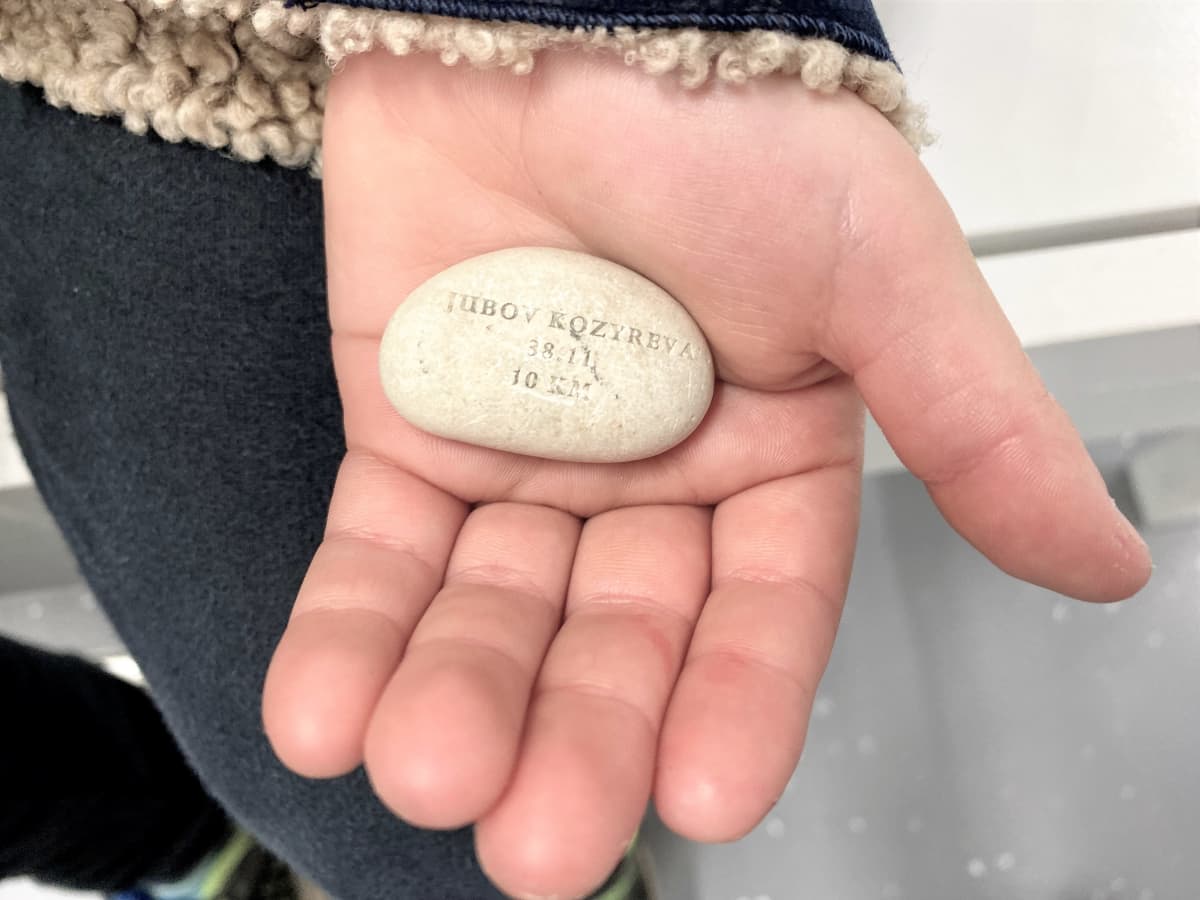 Lahden Hiihtomuseoon lahjoitettu kivi lapsen kämmenellä. Kivessä merkintöjä, jotka ovat osin kuluneet pois.