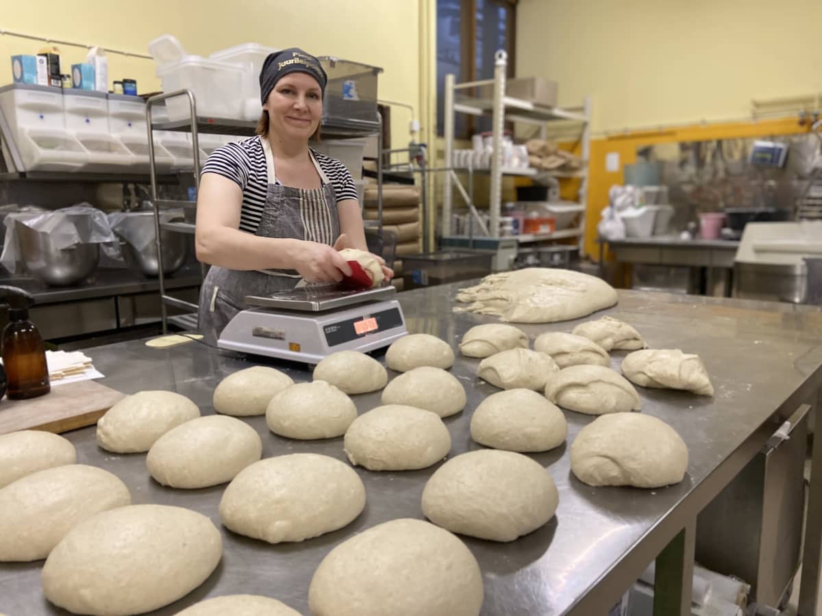 Pieni Juurileipomo-yrityksen omistaja, artesaanileipuri Kaisa Kinnari leikkaa ja punnitsee leipätaikinapaloja. Taikinapala on puntarin päällä. Edessä pöydällä on pyöriteltyjä leipätaikinapalleroita. 