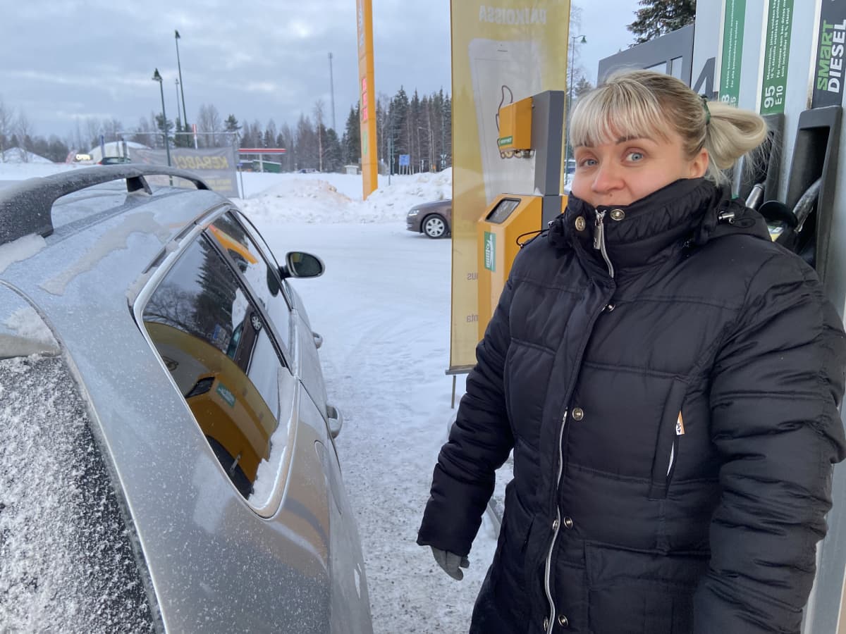 Anu Nousiainen Juvan ABC:llä henkilökuvassa. Vieressä hänen autonsa ja takana bensatankki.