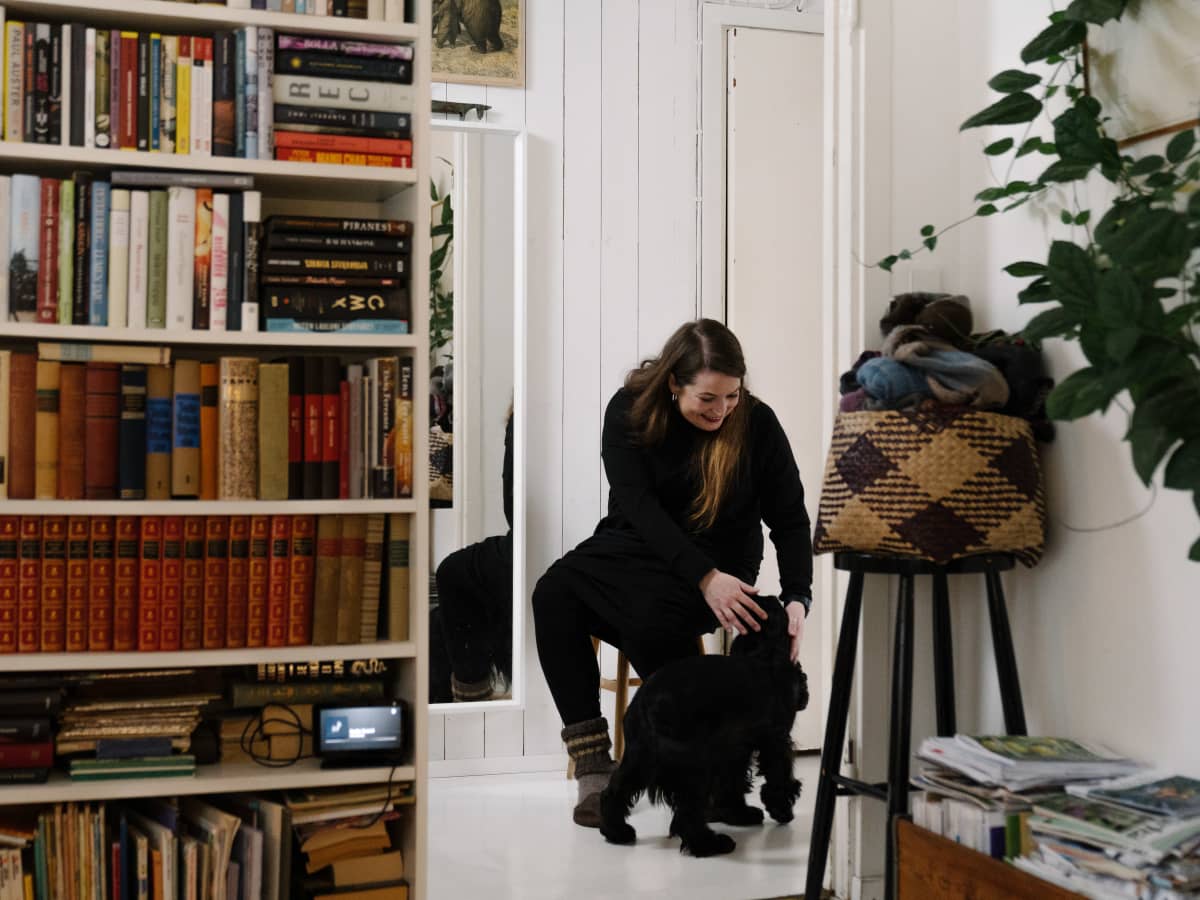 Marja Honkakorpi istuu kotinsa eteisessä koiransa kanssa.