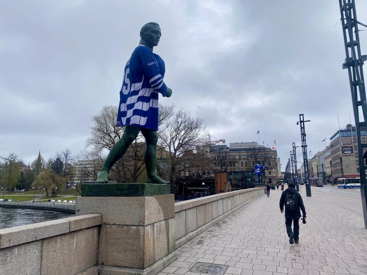 Tampereen Hämeenkadun sillan patsas, jolla Suomen pelipaita päällä. Sillalla kävelee muutama ihminen.