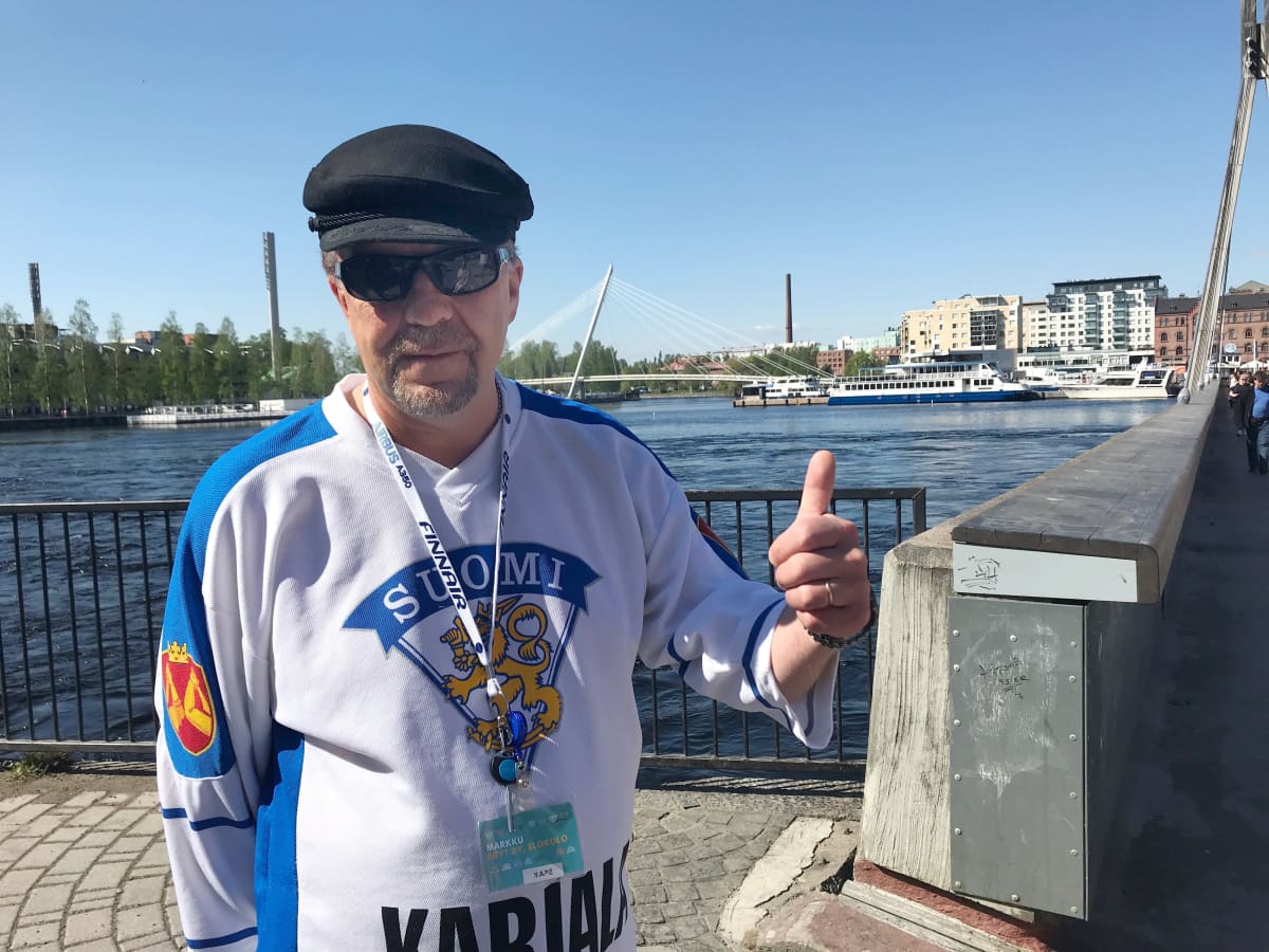 Mies Suomi-paita päällään ja aurinkolasit päässä näyttää peukkua kameralle. Takana näkyy Ratinan ja Laukontorin aluetta.