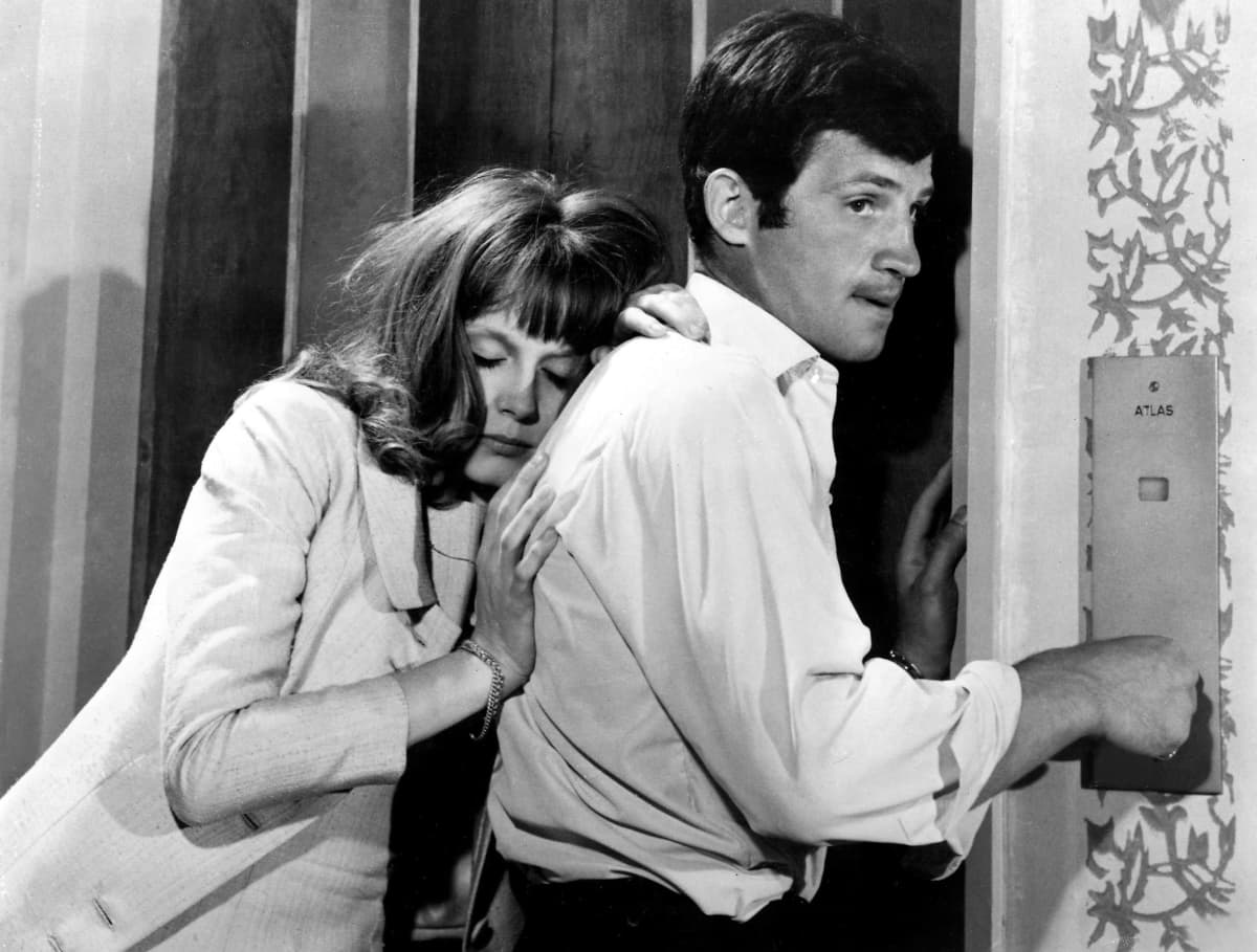 Dorléac ja Belmondo seisovat hissin ovilla. Dorléac nojaa Belmondon selkään. Belmondo painaa hissin nappulaa keskittyneen näköisenä