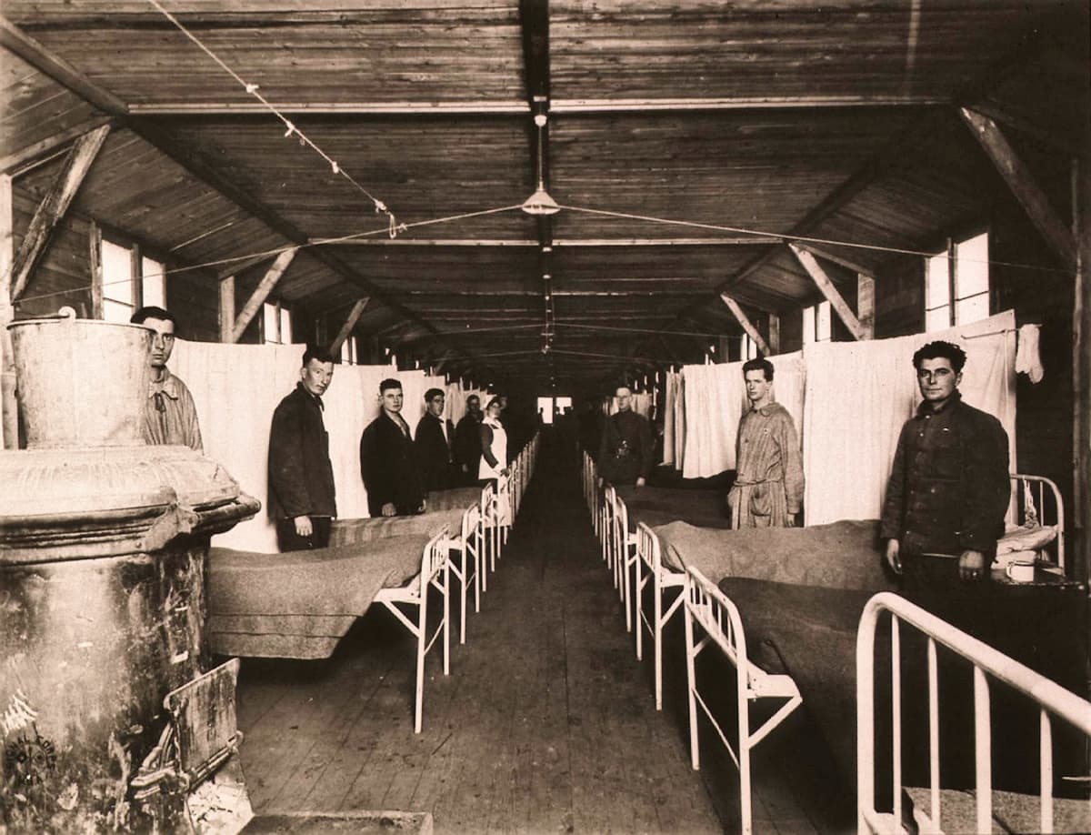 Mustavalkoinen kuva, jossa sairaalasänkyjen jono ja sänkyjen vieressä miehiä univormuissa.