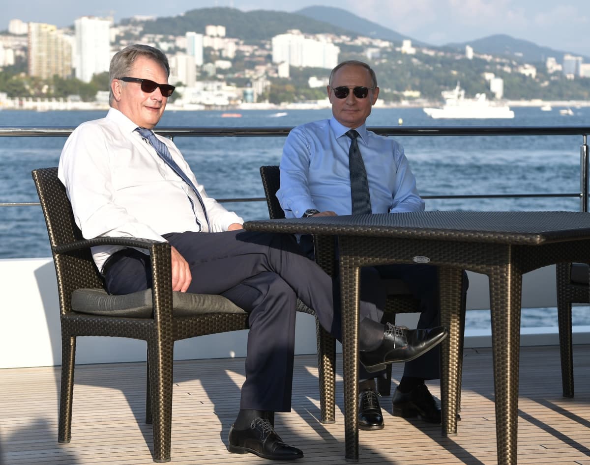 Suomen presidentti Sauli Niinistö ja Venäjän presidentti Vladimir Putin istuvat pöydän ääressä auringonpaisteessa Putinin veneellä.