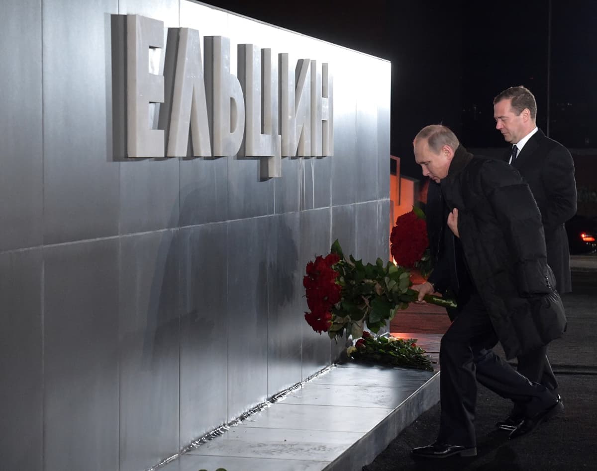 Putin ja Medvedev laskevat punaisia ruusuja metallisen seinämän eteen. Seinämässä lukee suurilla kohokirjaimilla "Jeltsin".