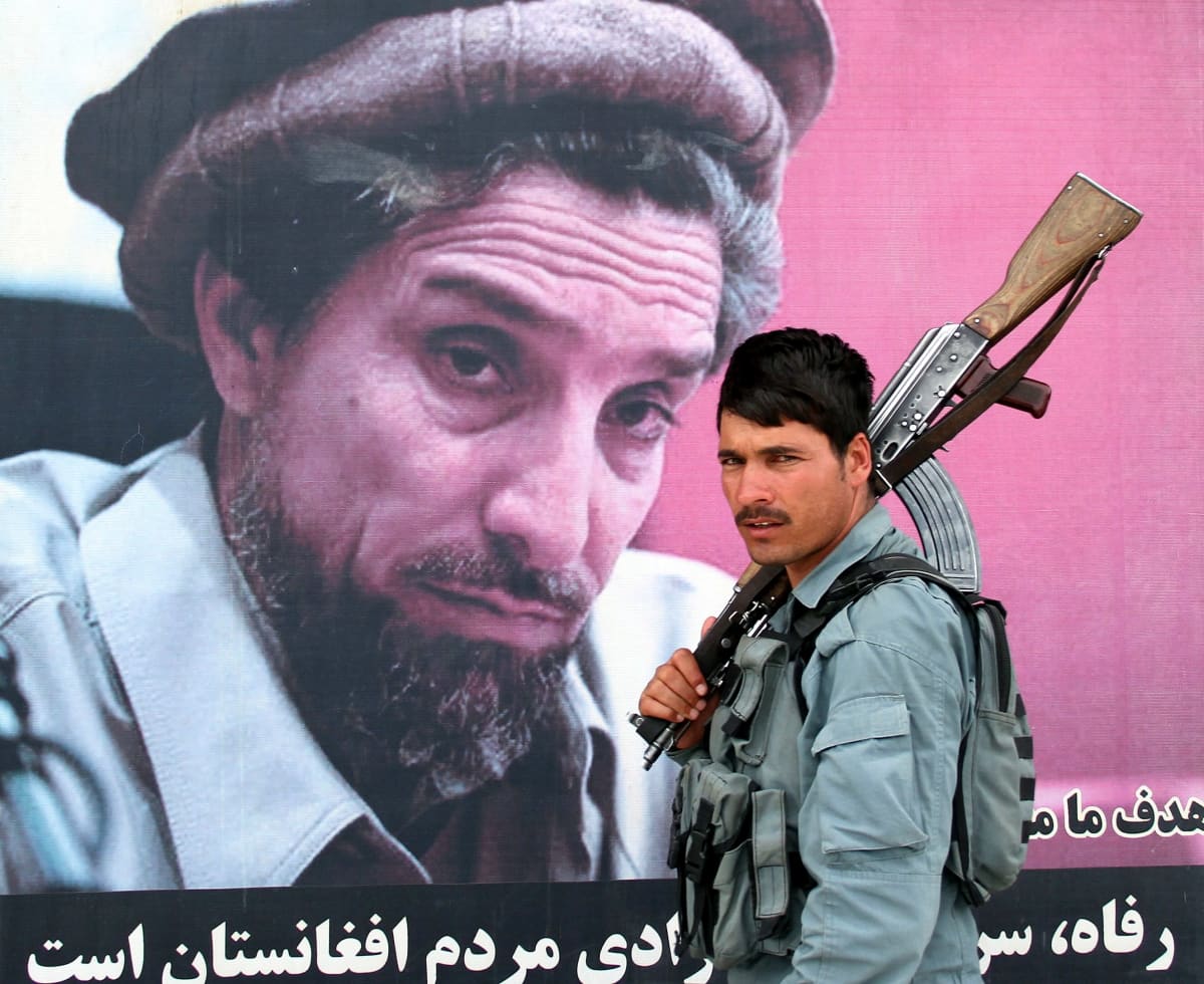 Rynnäkkökivääriä olallaan piipusta kiinni pitäen kantava mies ohittaa suurta kuvaa, joka esittää Ahmad Shah Massoudia. Sotilas katsoo kameraan päin. Massoudin kuva tuntuu ikään kuin katsovan sotilasta.