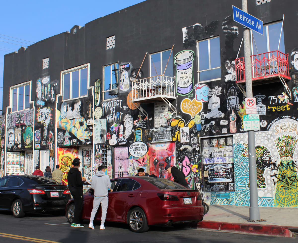 Neljä miestä juttelee autossa istuville henkilöille graffitin täyttämän rakennuksen vieressä.