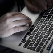 Miehen kädet kannettavan tietokoneen näppäimistöllä.