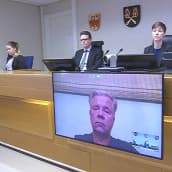Kuva oikeussalista, jossa tuomarit kuuntelevat vastaajaa videoyhteyden kautta