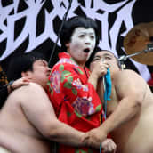 Japanin esityksessä kaksi sumopainijaa rutistaa neulovaa geishaa.