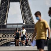 Ihmisiä suojamaskeissaan Eiffel-tornin juurella
