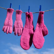 Pinkit villasormikkaat ja -sukat on ripustettu narulle kuivumaan. Takana sinistä taivasta.