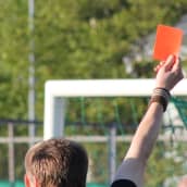 Kuvassa jalkapallotuomarin käsi on nostanut punaisen kortin ilmaan. 