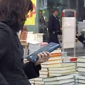 Nainen lukee kirjan takakantta kirjakaupassa